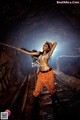 A woman in an orange outfit holding a rifle in a cave.