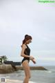 A woman in a black bathing suit walking on the beach.