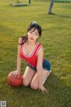 A woman sitting on the grass with a basketball.