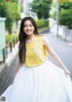 A woman in a yellow top and white skirt posing for a picture.