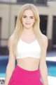 A woman in a white top and pink skirt posing by a pool.